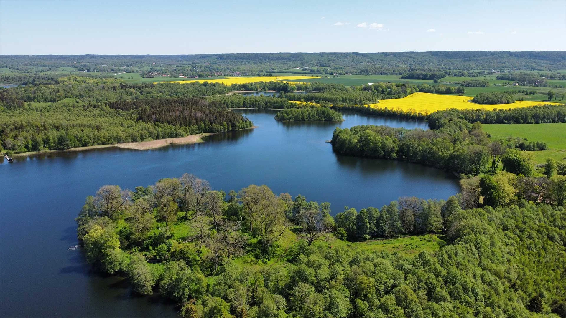 Gräsbevuxna ruiner av medeltidsborgen Axevalla hus i ett lummigt naturlandskap vid Husgärdessjön i Skara.