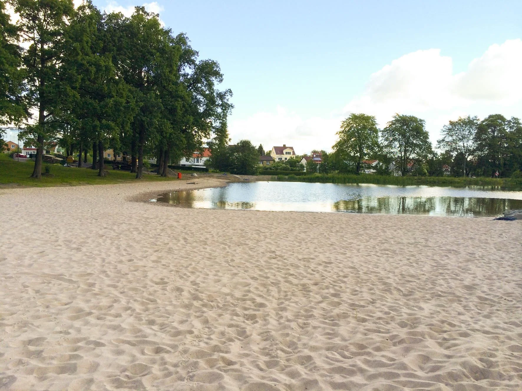 Badplatsen vid Boulognersjön i Skövde med badbrygga och gröna omgivningar en solig sommardag.