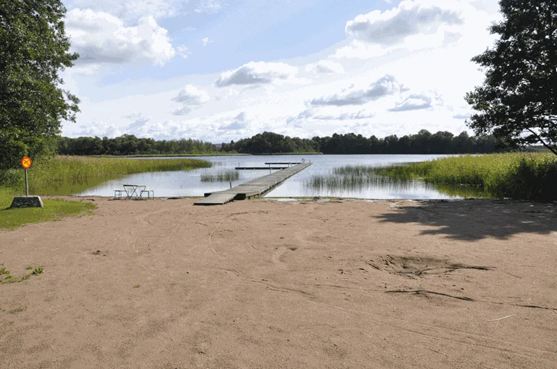 Sandstrand och badbrygga vid Näsbadet i Vallebygden nära Skara en solig sommardag.