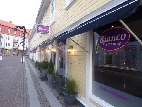 Exterior of restaurant Bianco in a yellow wooden building along a cobblestone street in Skara.