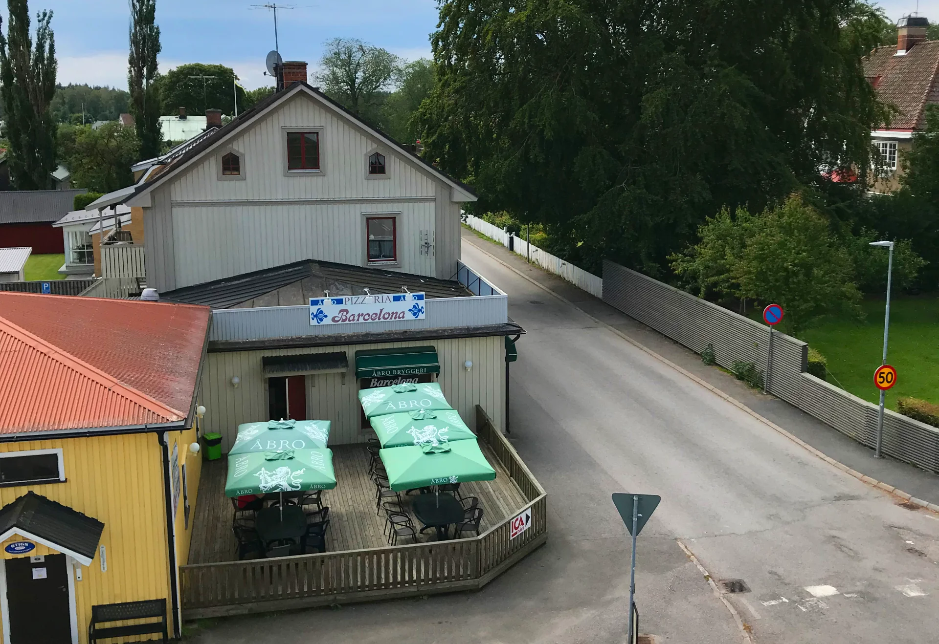Exteriör av Pizzeria Barcelona i Axvall med uteservering och skyltning under en klar sommardag.