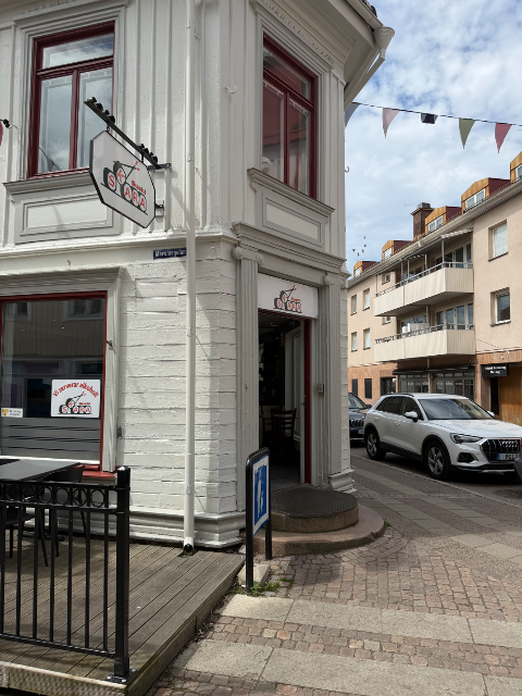 Vit trähusfasad med skylt för en sushirestaurang i ett gathörn med kullersten.